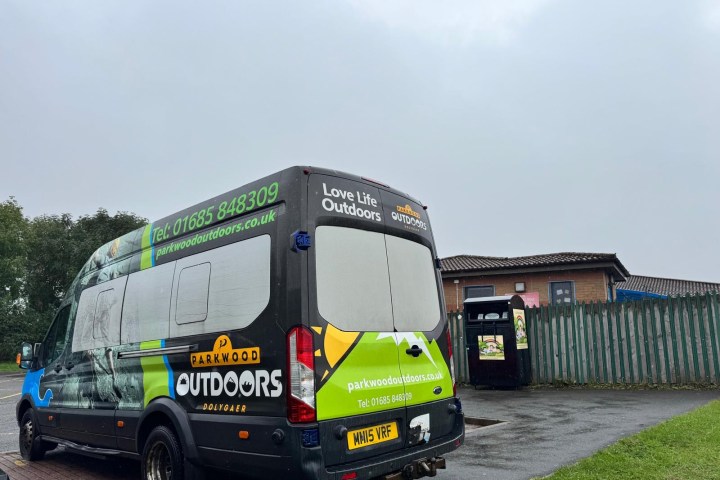 Parkwood Outdoors van parked near a building and fence on a cloudy day.
