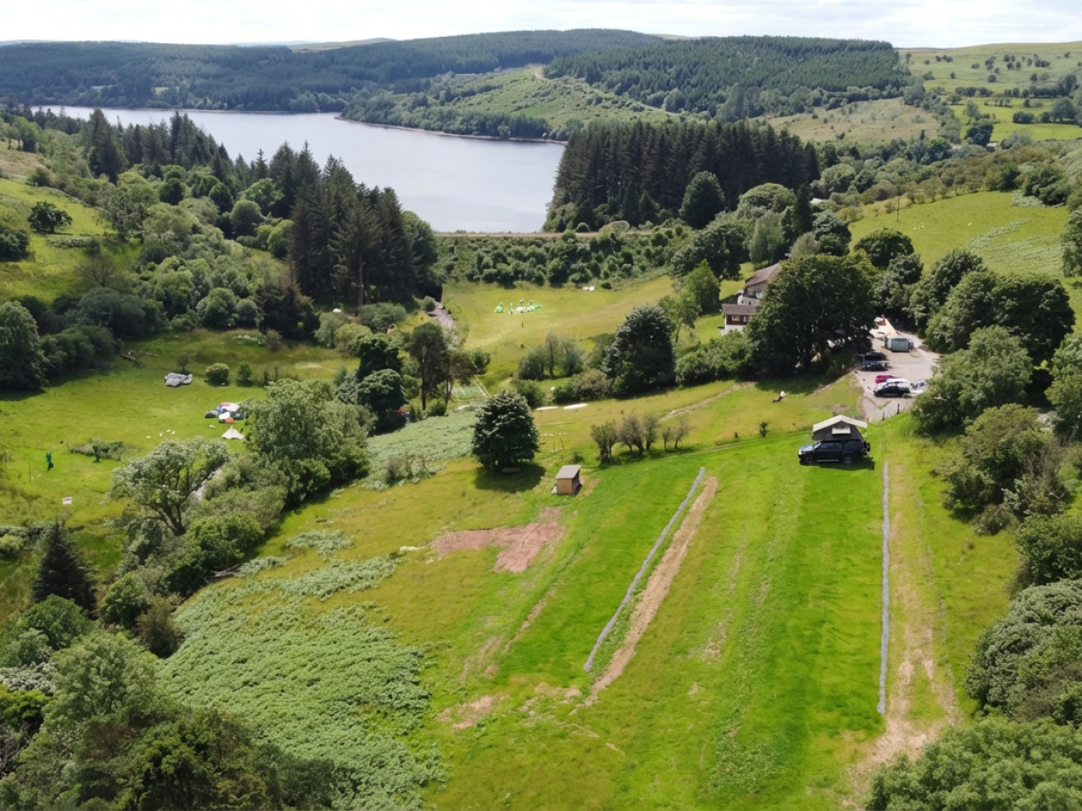 Aerial view of lush green landscape, cottages, and a lake surrounded by hills and trees.