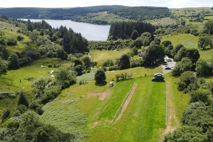 Aerial view of lush green landscape, cottages, and a lake surrounded by hills and trees.