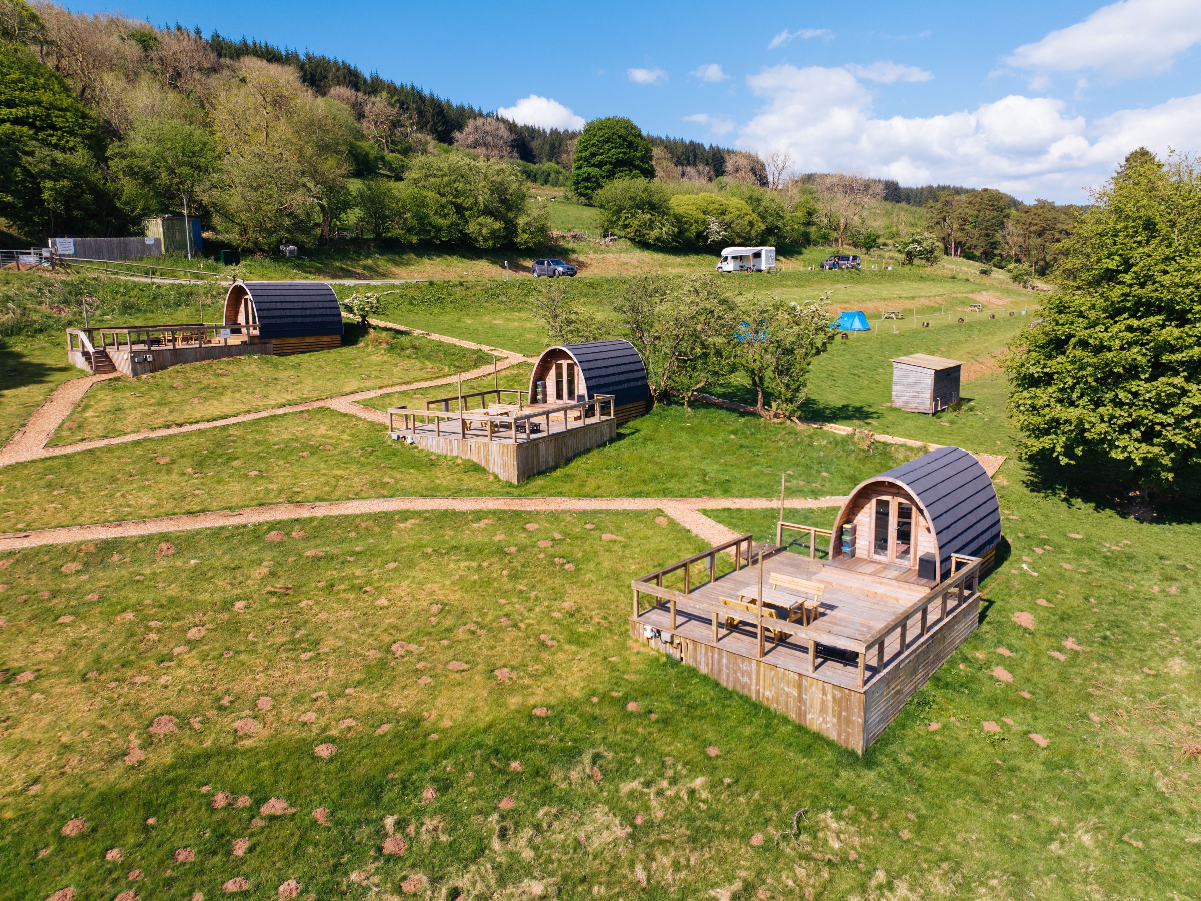 Aerial view of three wooden camping pods on grassy terrain with paths.