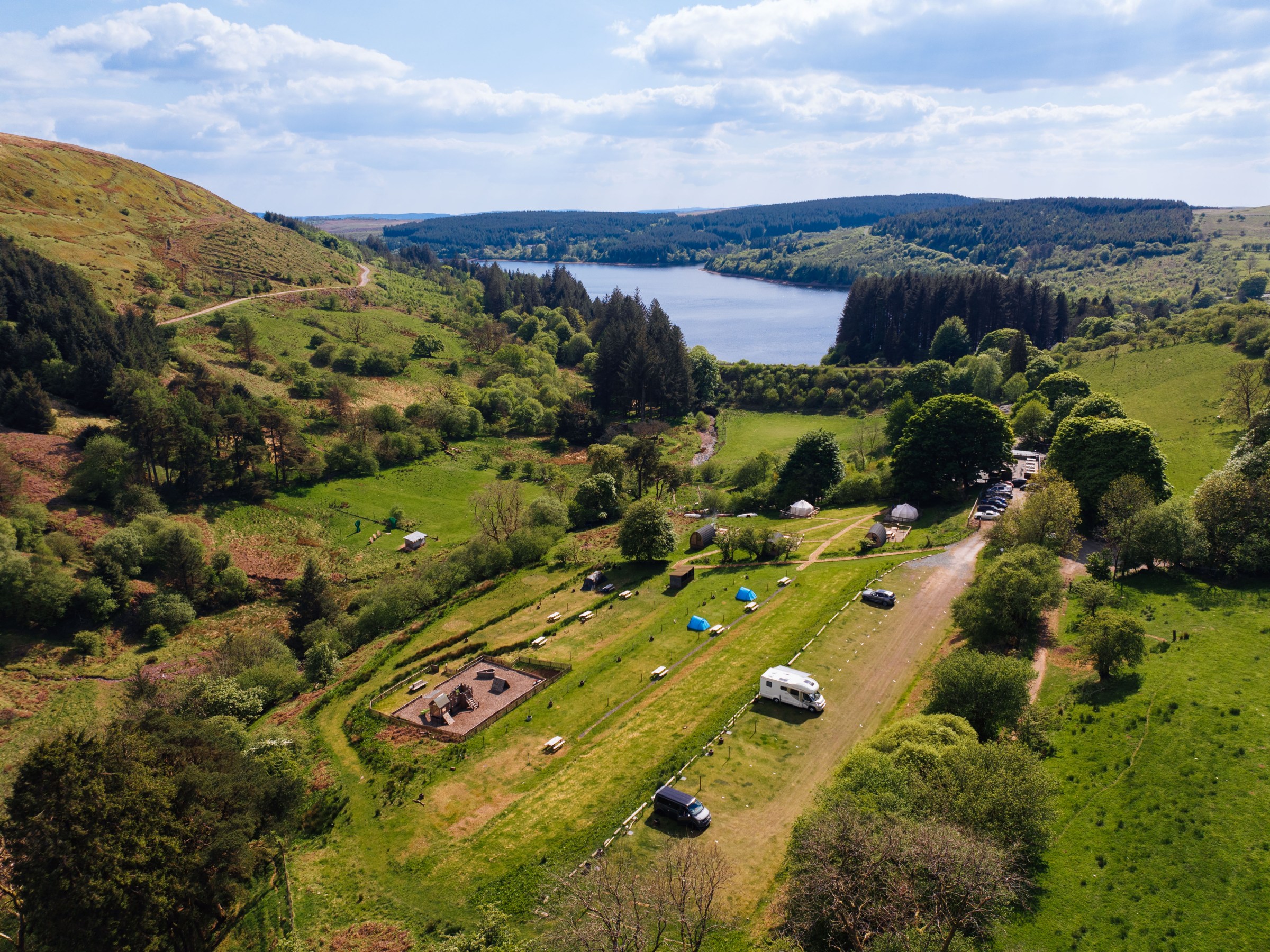 Aerial view of a campsite near a lake surrounded by hills and trees.