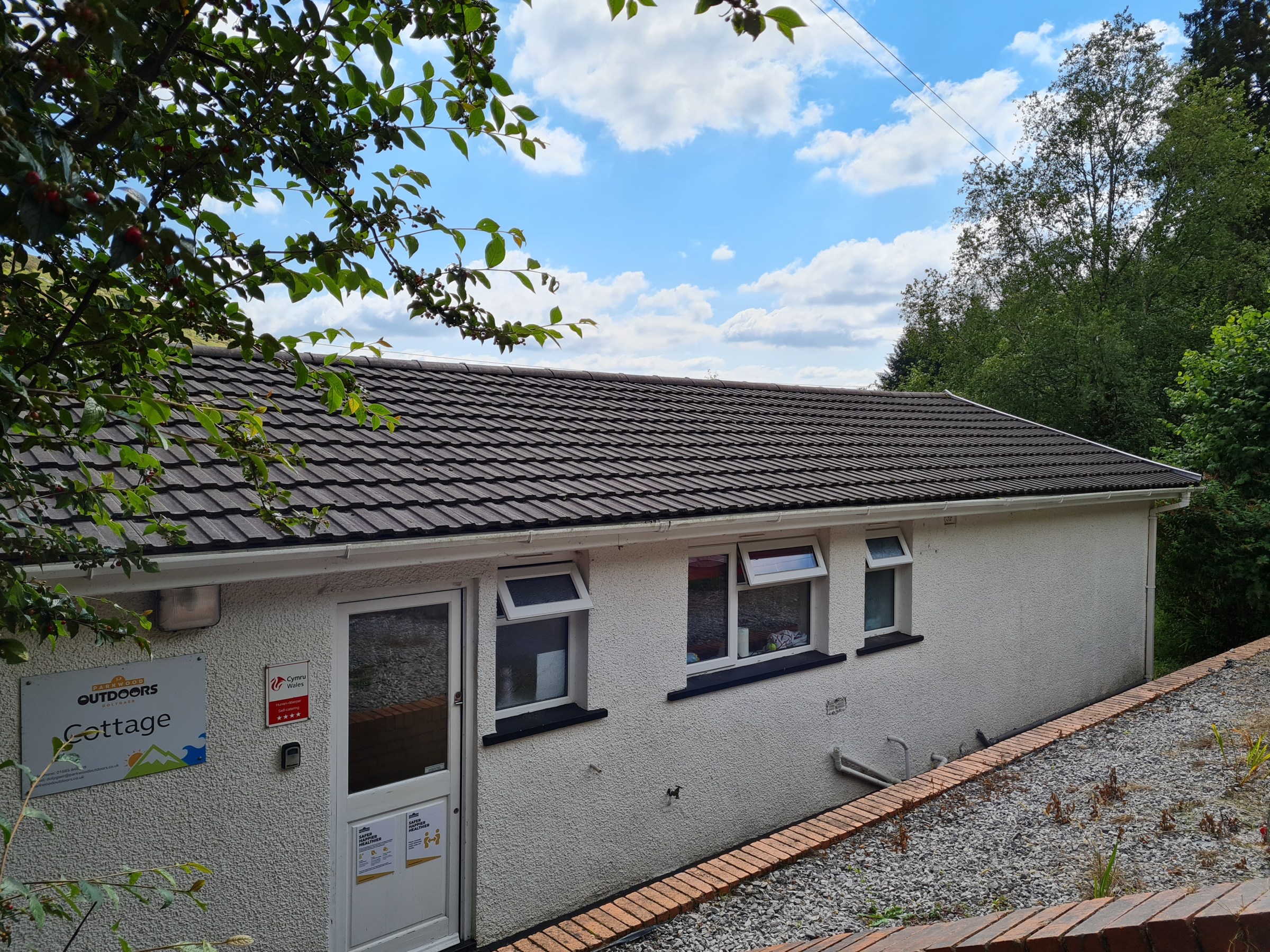 Small white building with a gray roof, surrounded by trees and a clear sky.