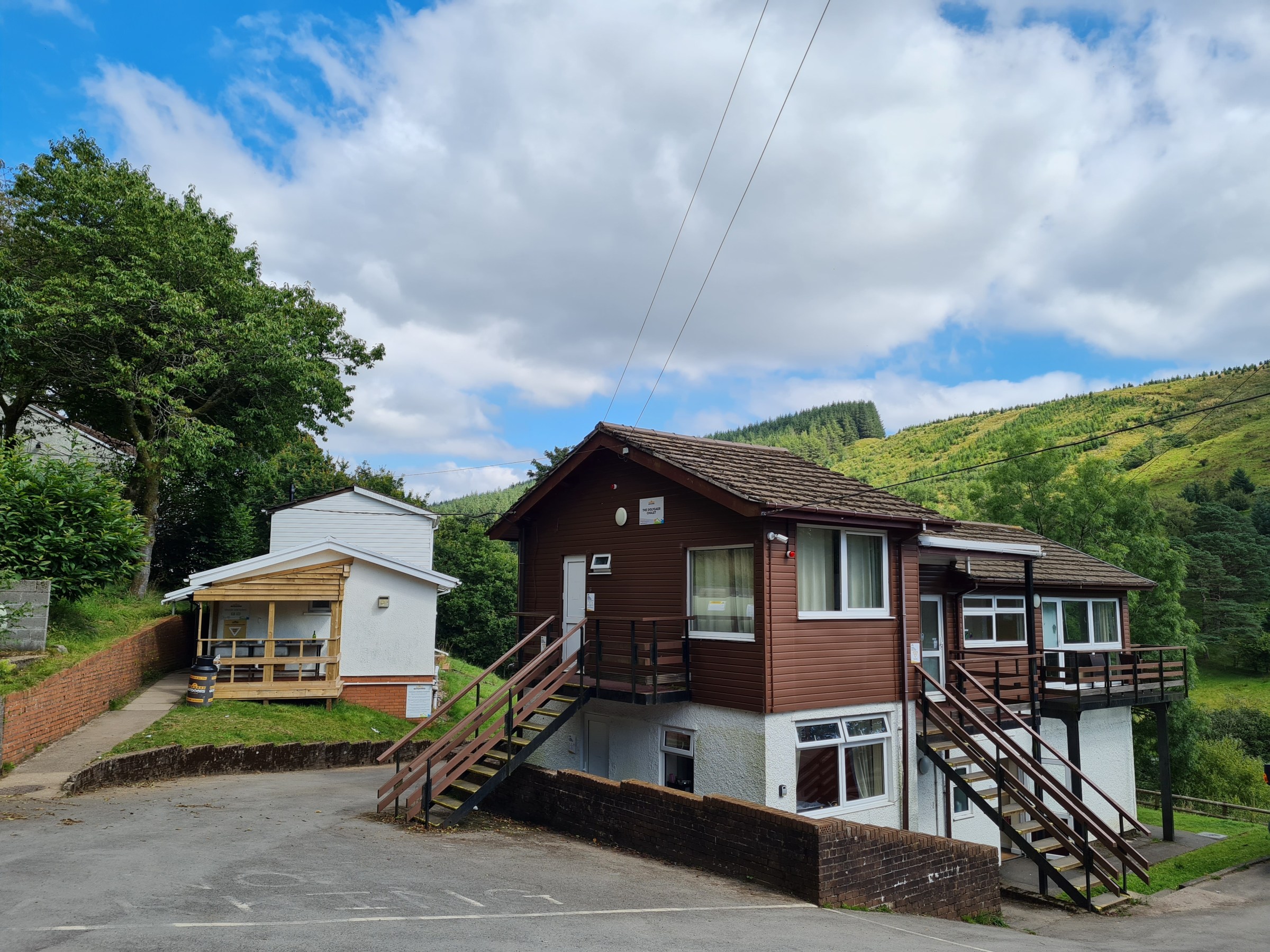 Wooden house with stairs, trees, and cloudy sky in the background.