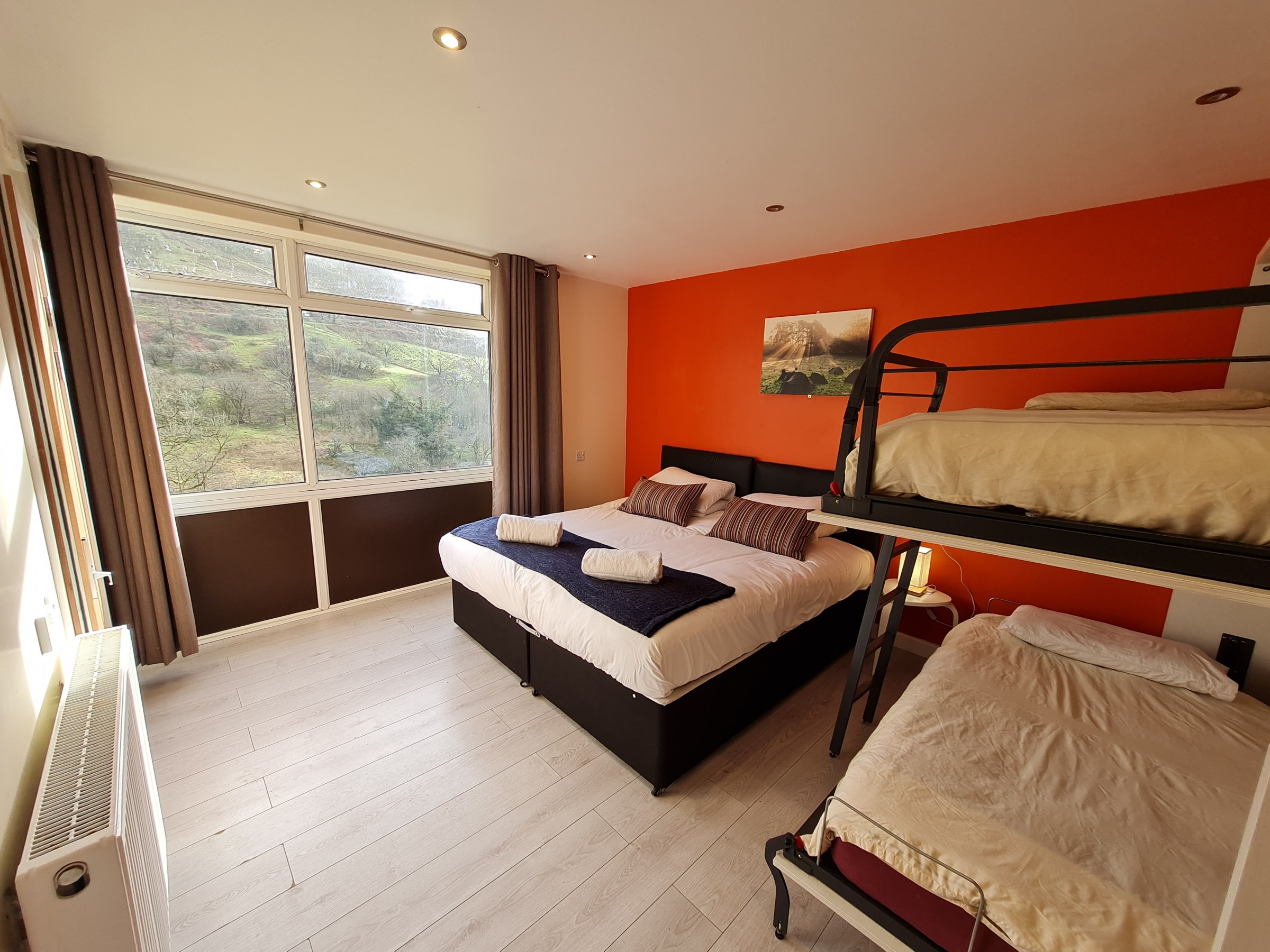 Bedroom with a double bed, bunk bed, orange wall, and large window with a scenic view.