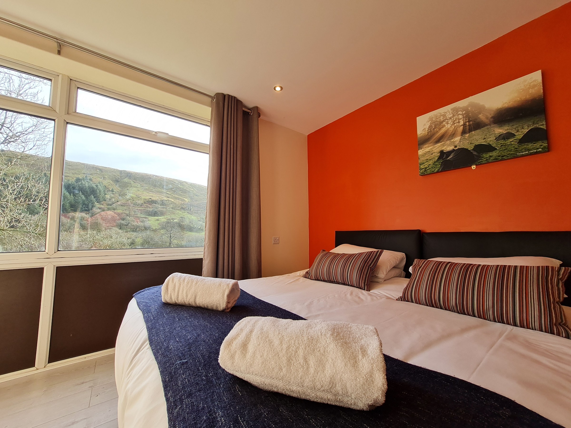 Cozy bedroom with large window, orange accent wall, and two neatly made beds.