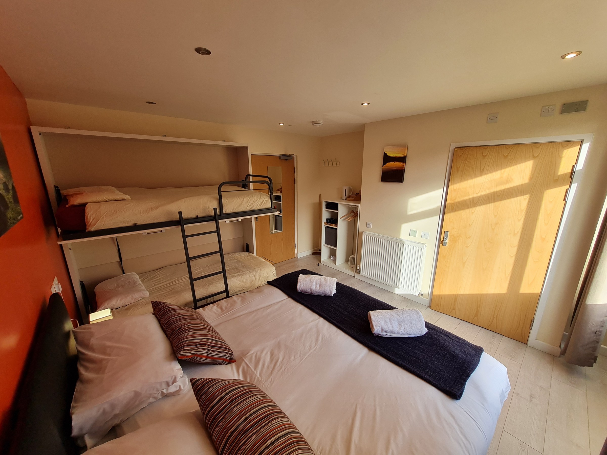 Hotel room with double bed, bunk beds, and folded towels on each bed.