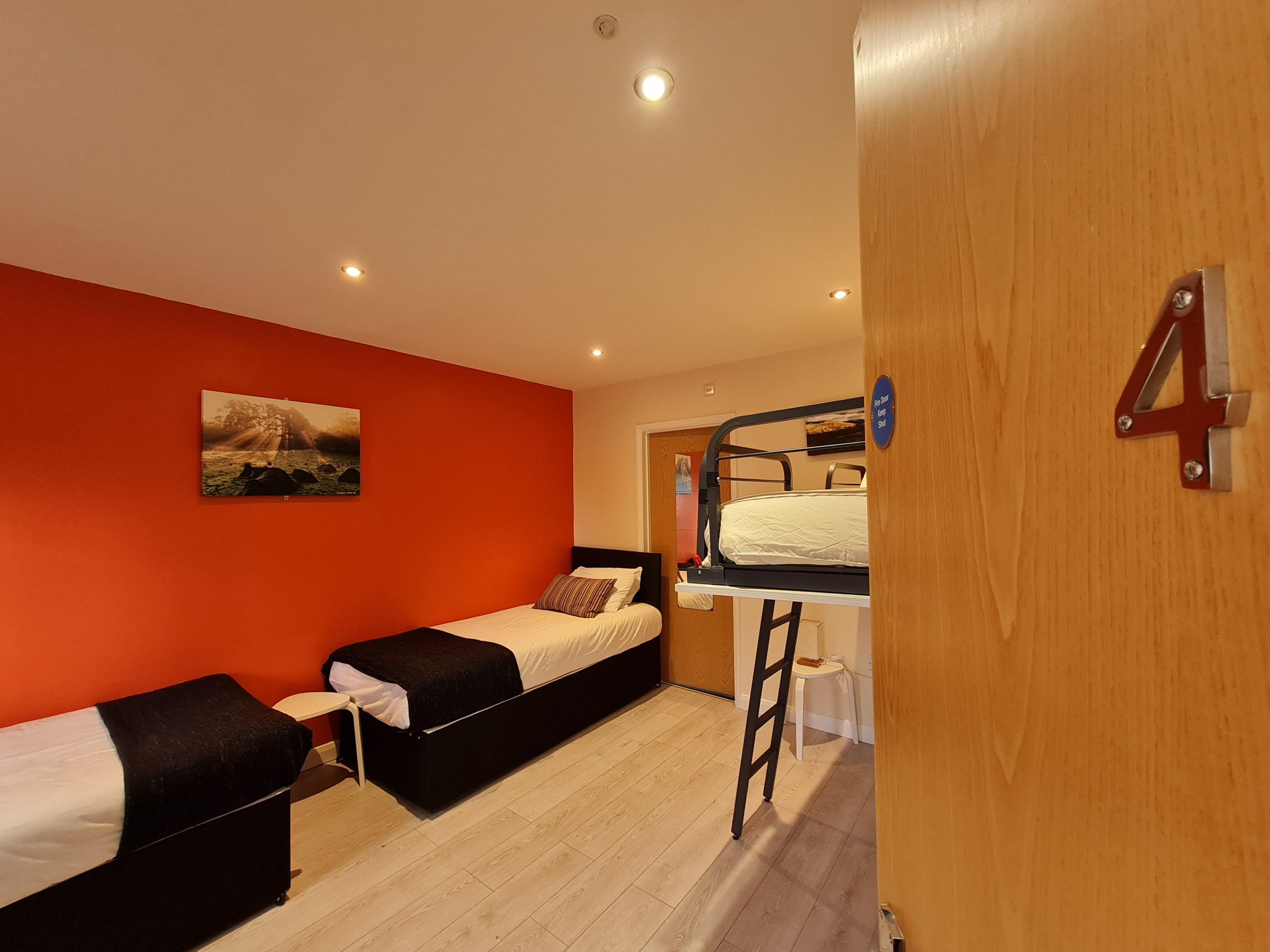 Room with two beds and a bunk bed, red accent wall, and wooden floor.