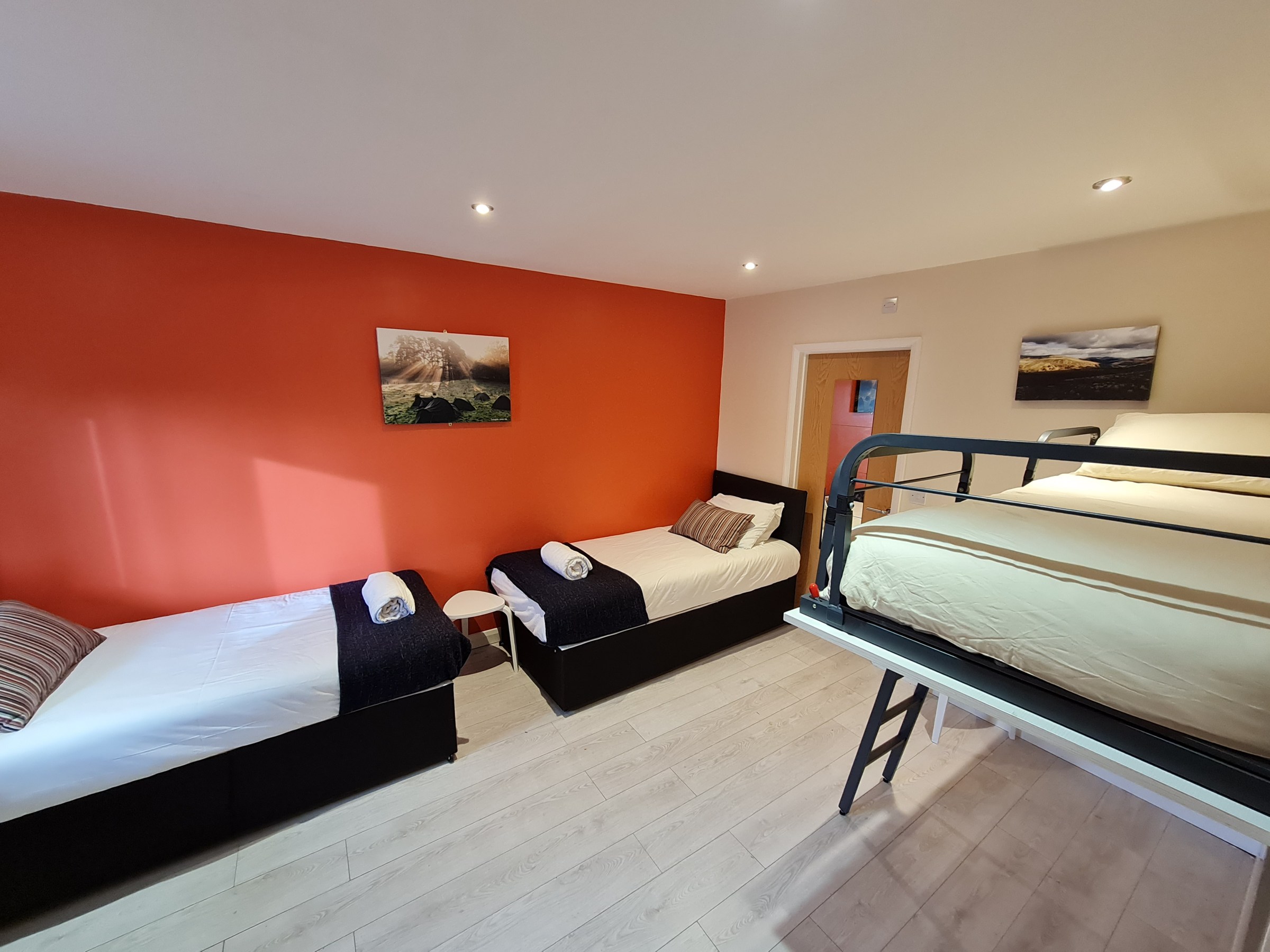 Room with two single beds, one bunk bed, orange wall, and landscape paintings.