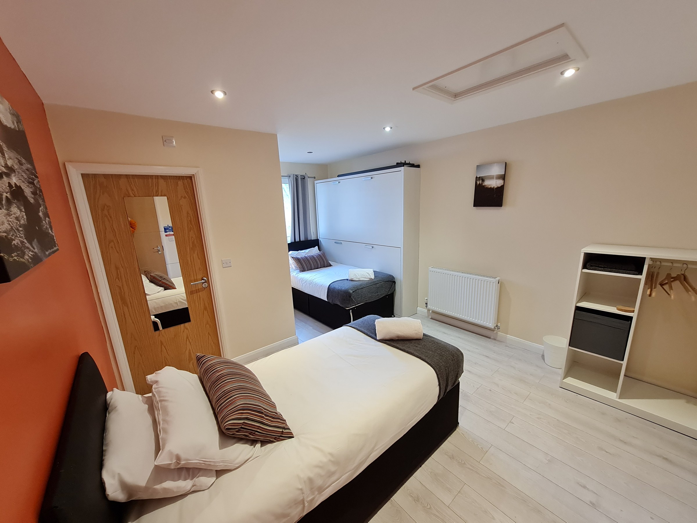 Cozy bedroom with two beds, orange accent wall, and wall art.