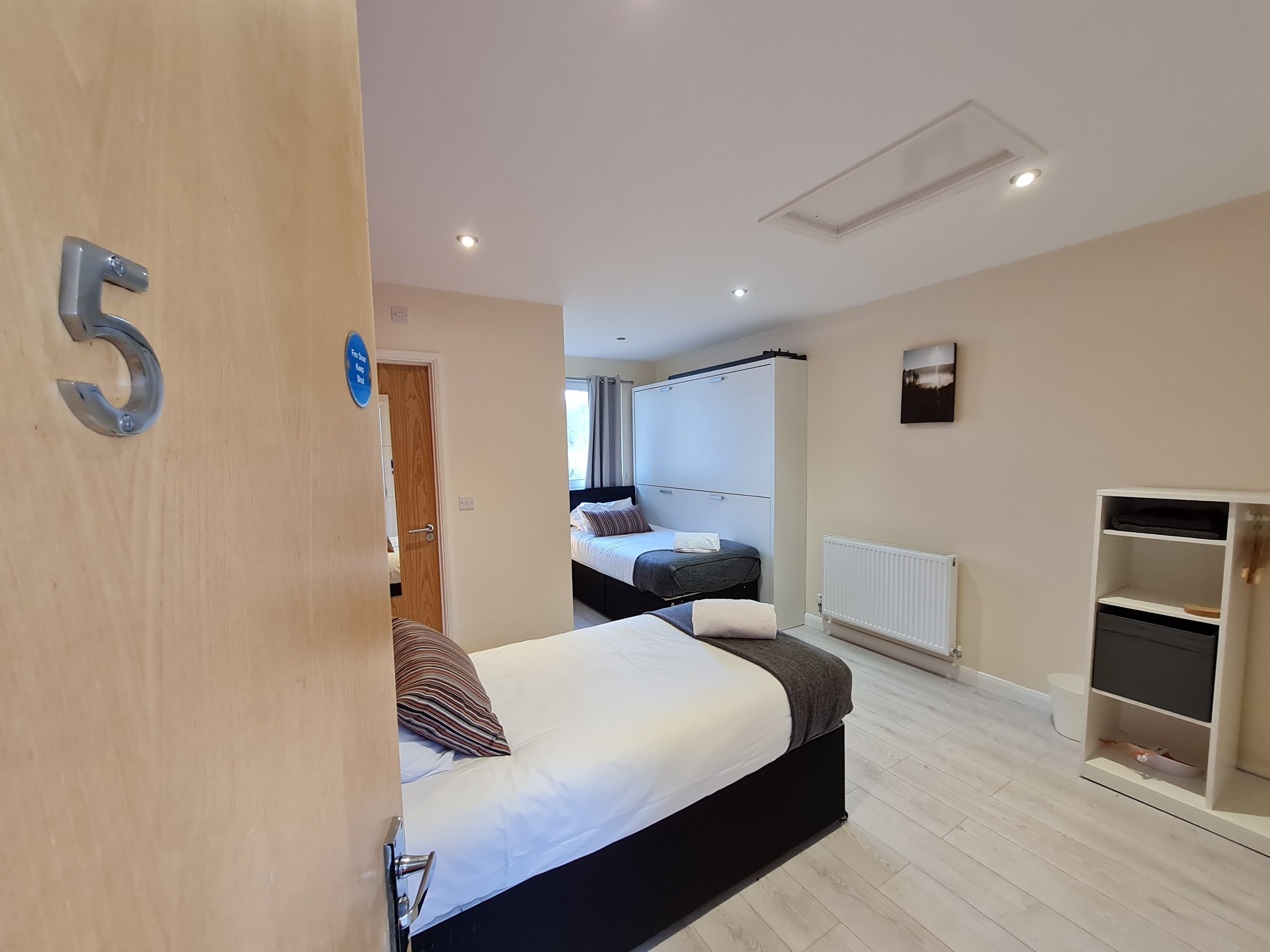 Hotel room with two beds, open door, and wooden flooring.