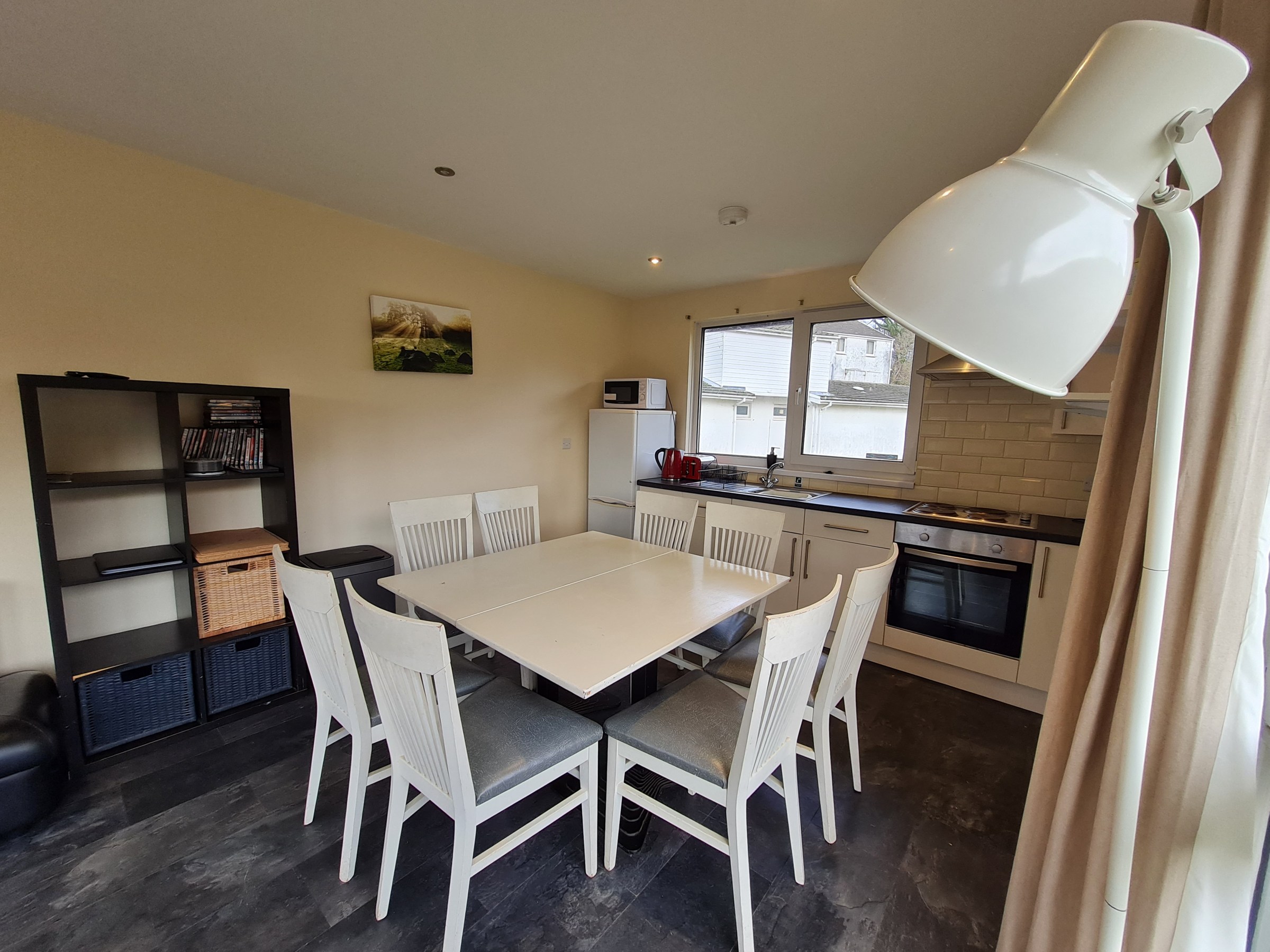 Modern dining area with white chairs, table, and kitchen appliances.