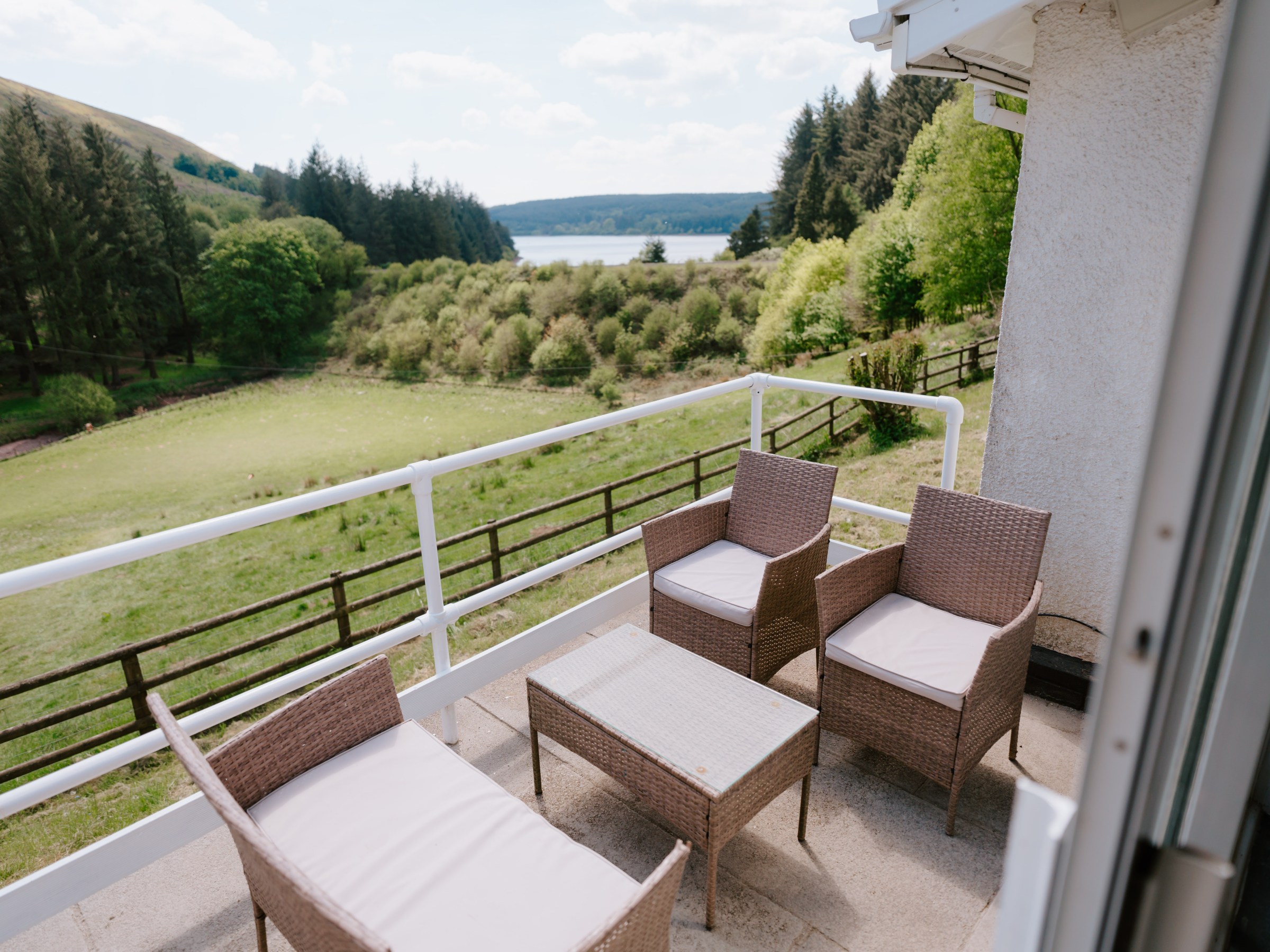 Balcony with wicker furniture overlooking a lush landscape and distant lake.