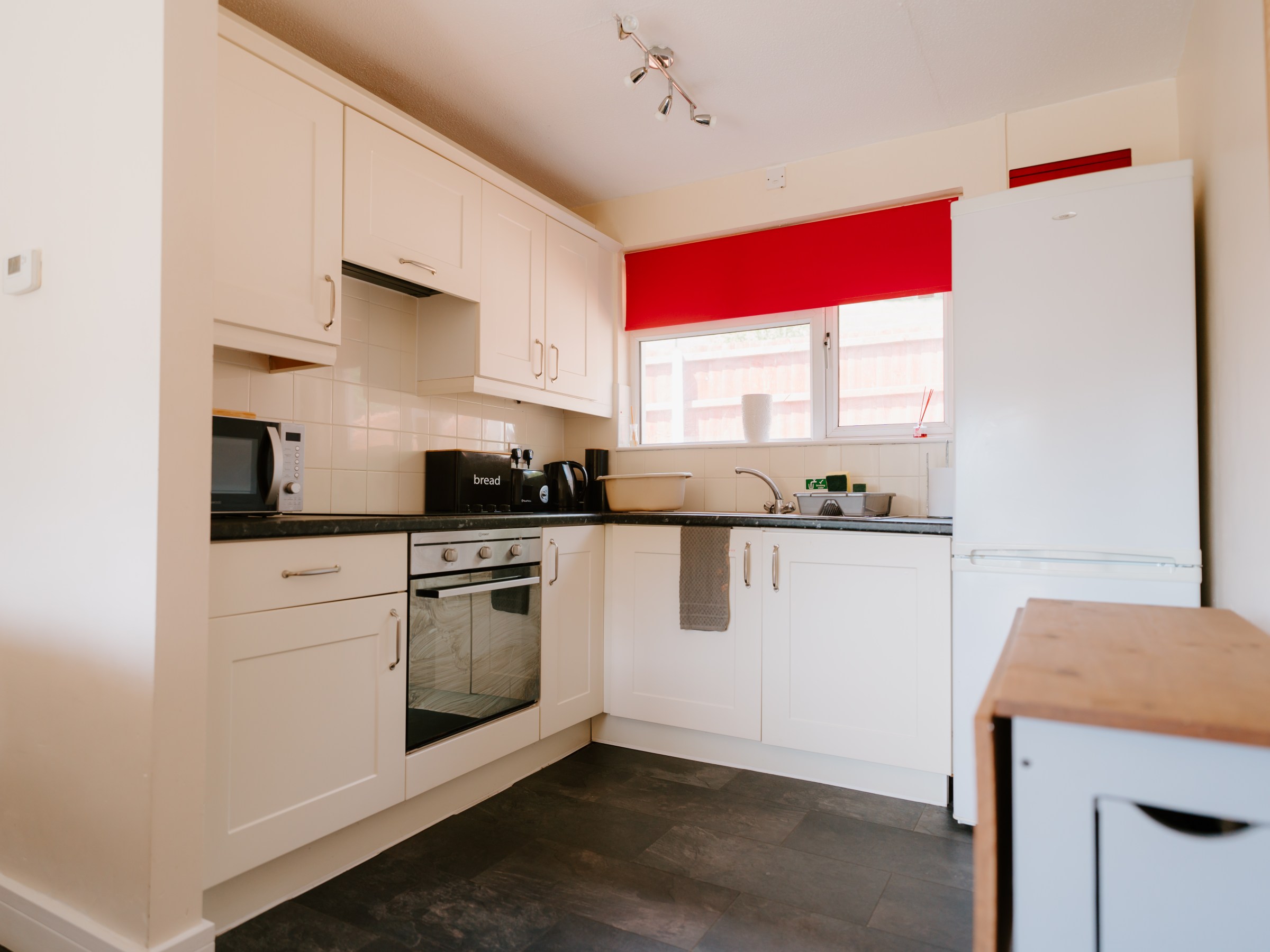 Modern kitchen with white cabinets, red blind, oven, and fridge.