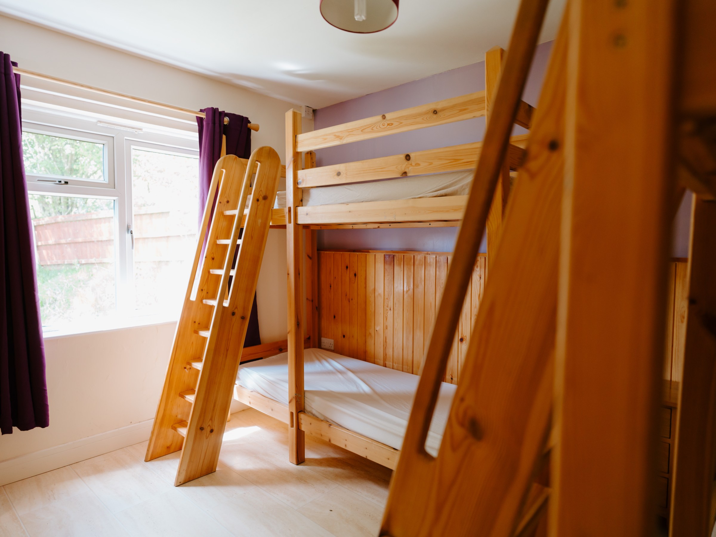 Room with wooden bunk beds and purple curtains.