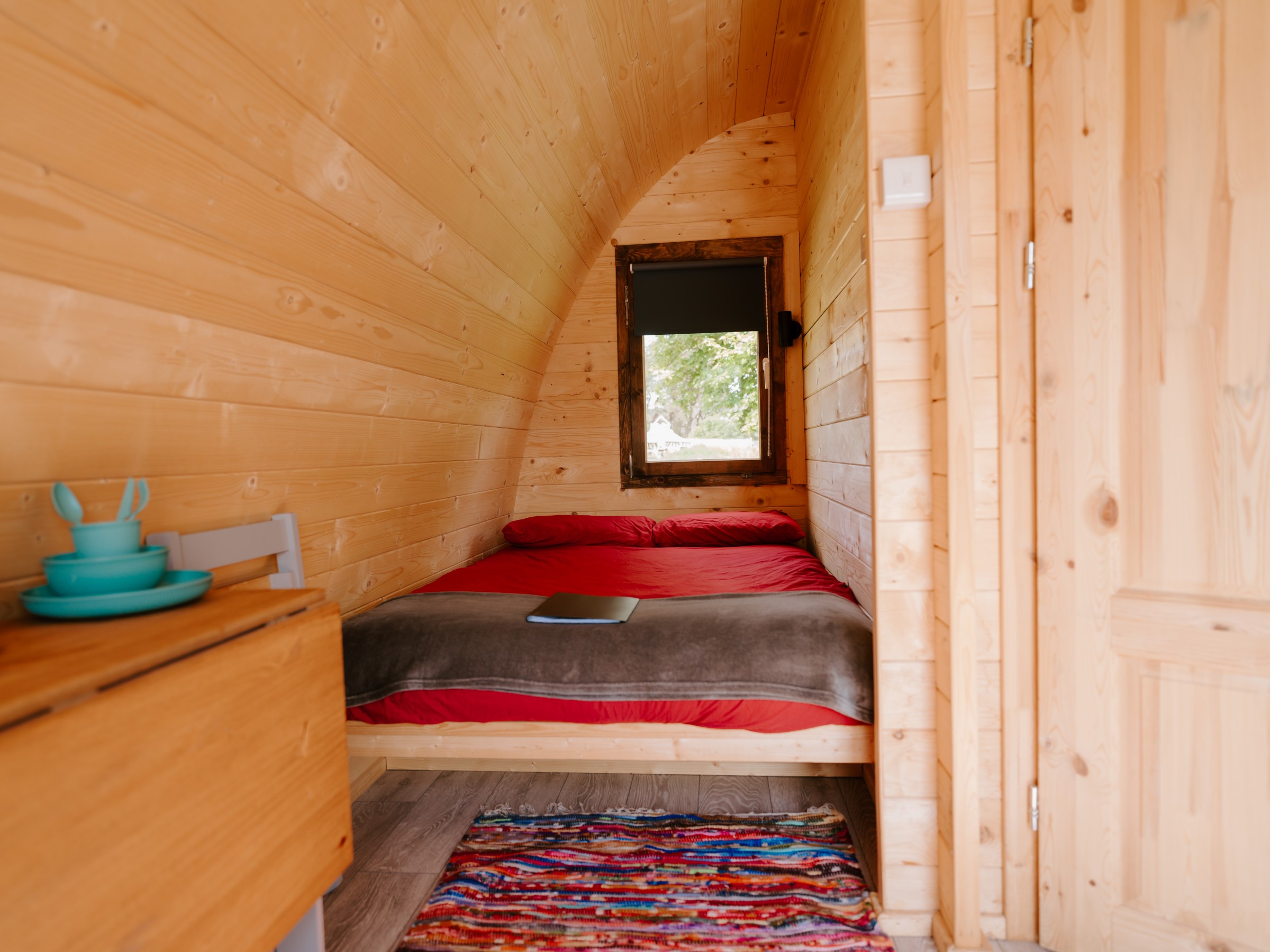 Cozy wooden cabin interior with bed, table, and colorful rug.