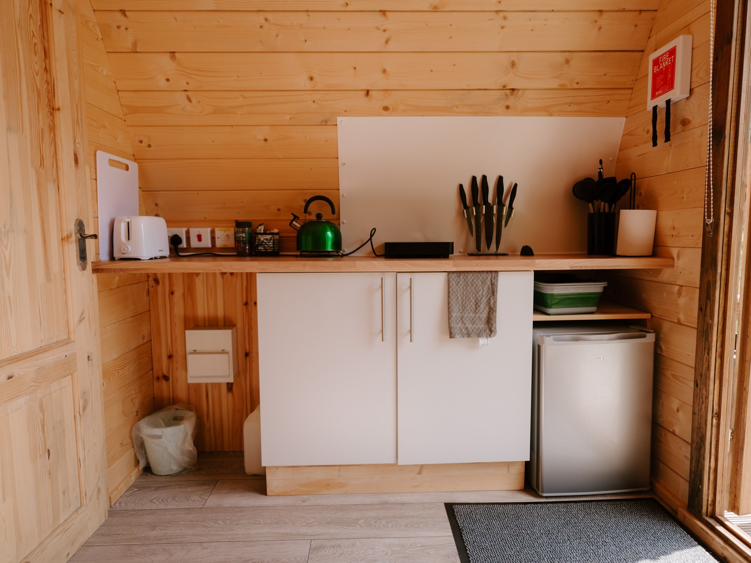 Small wooden kitchenette with a kettle, knives, and mini fridge.
