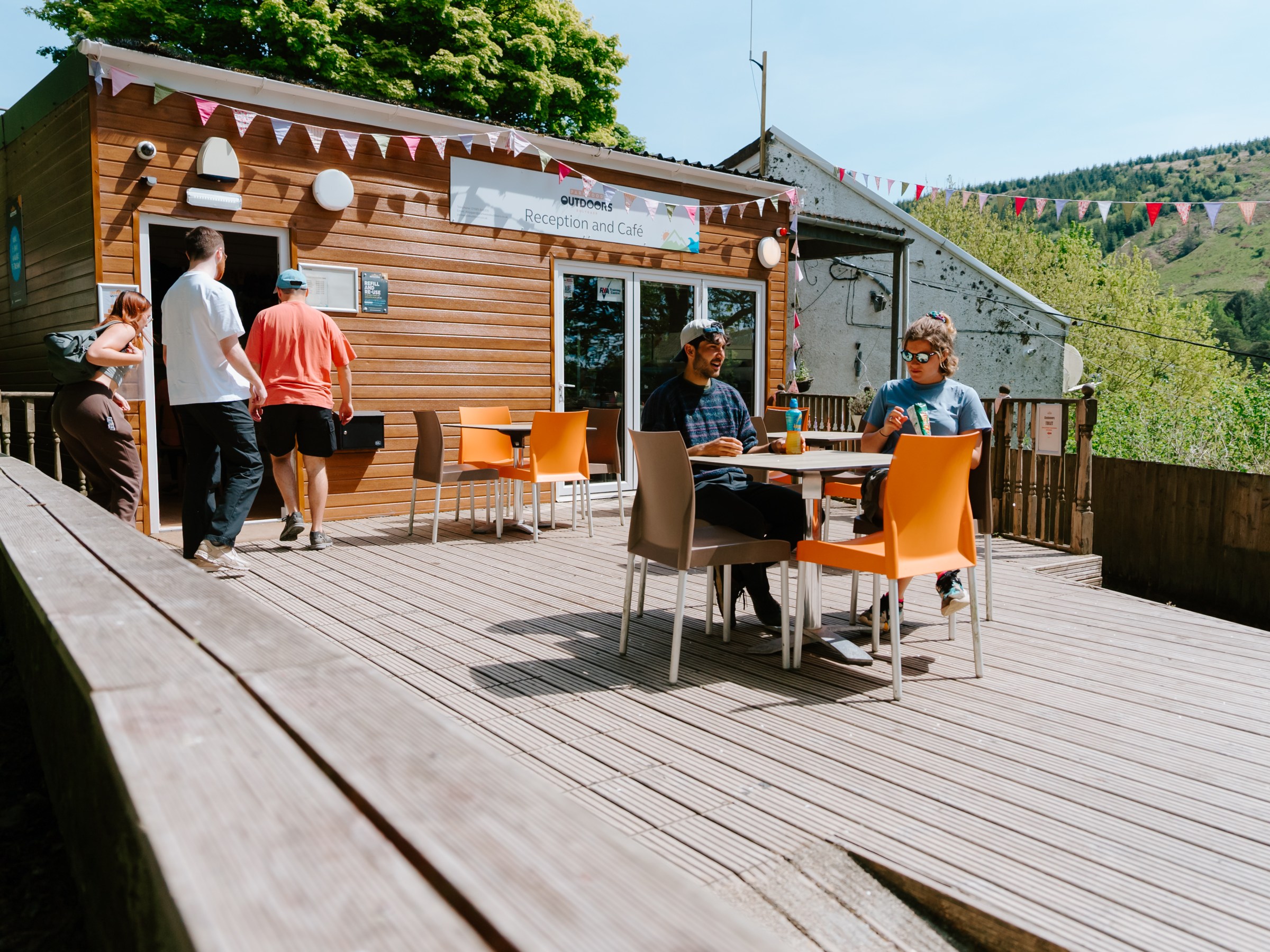 People sitting outside a café with orange chairs and wooden exterior on a sunny day.