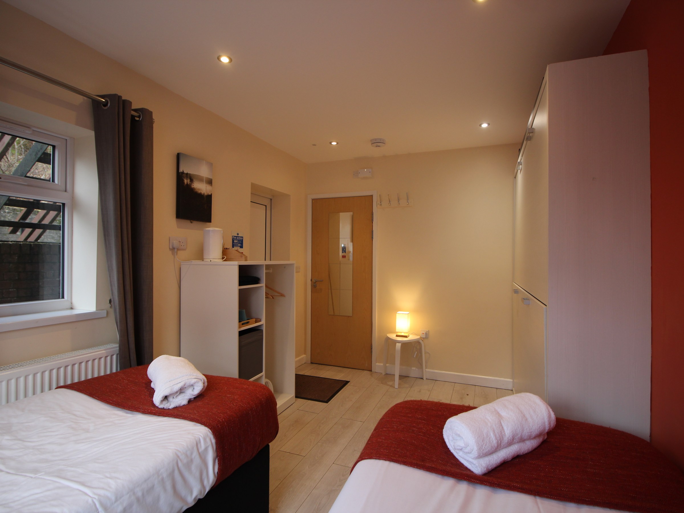 Cozy room with two red-covered beds, a small table lamp, and wooden door.