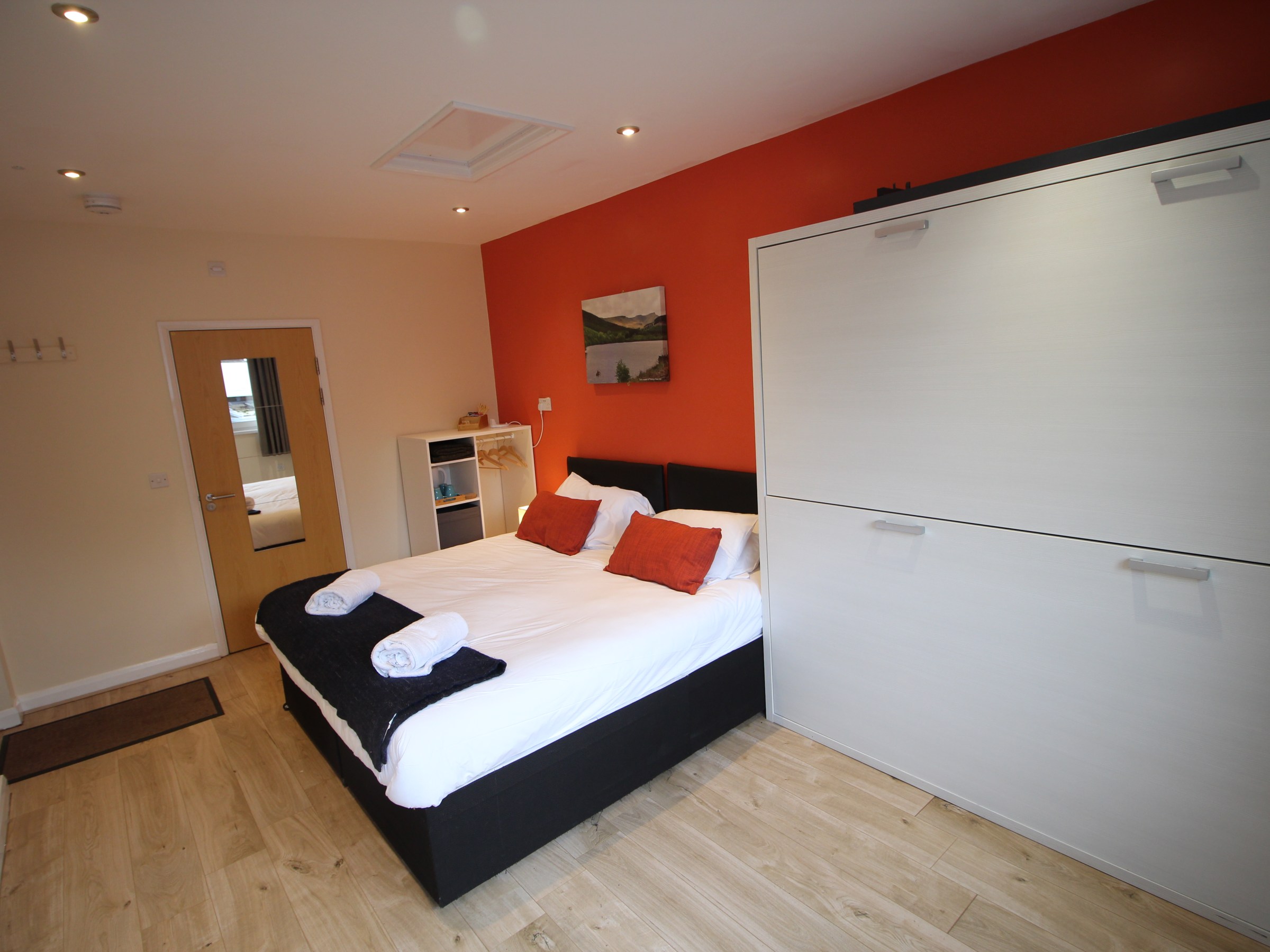 Modern bedroom with a double bed, orange accent wall, and fold-down desk.